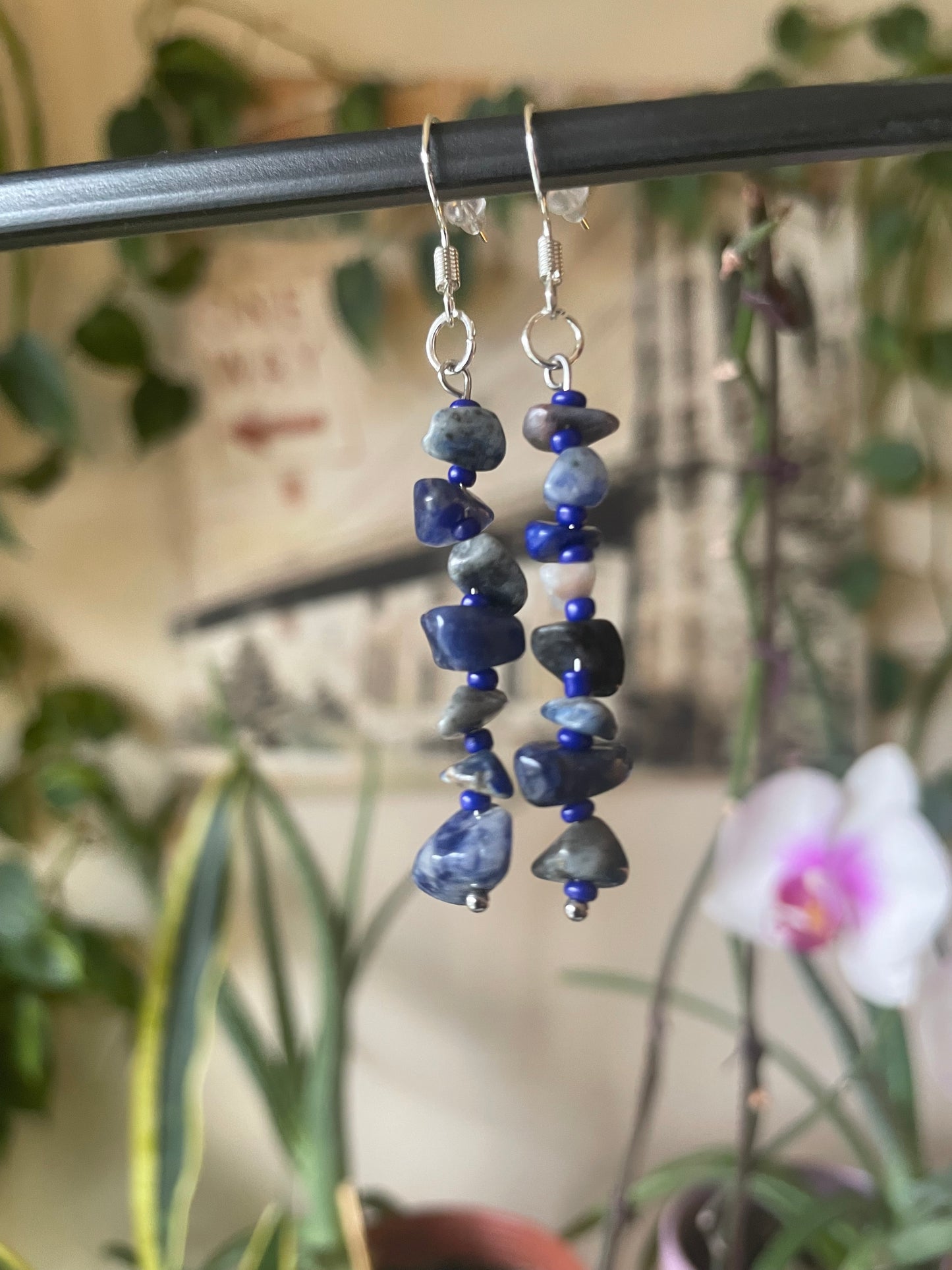 Blue beaded earrings on a stand with a blurred plant background