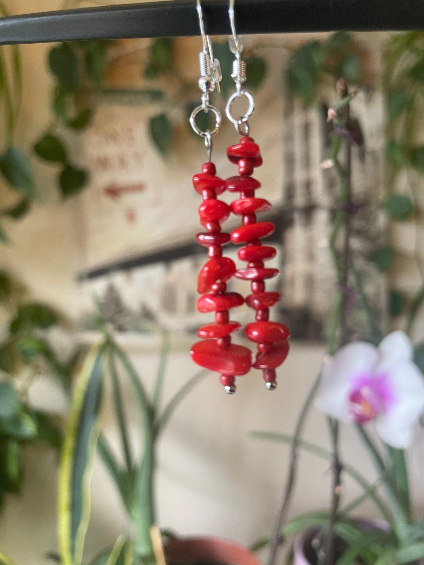 Red beaded earrings with a blurred background of plants