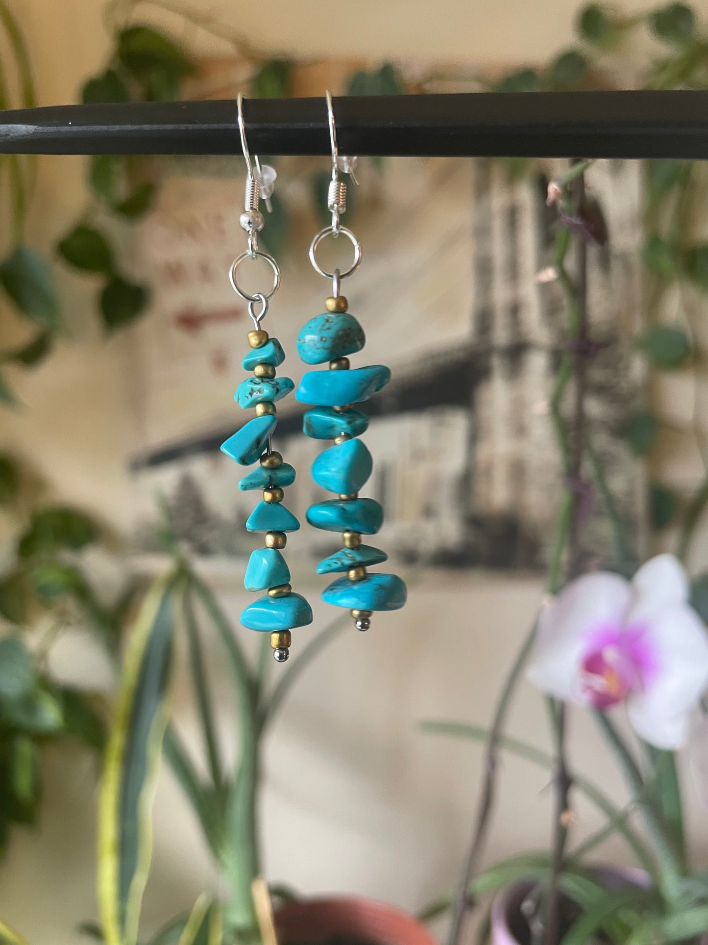 Turquoise beaded earrings on a stand with a blurred background of plants.